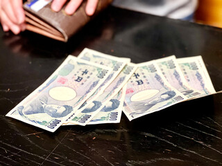 テーブルの上に置いた数枚の千円札と財布を持つ手