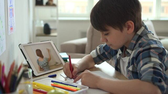Home education for children. Brunet child in blue shirt draws at art lesson with tutor by video conference spbas spbd via tablet at table in light room closeup