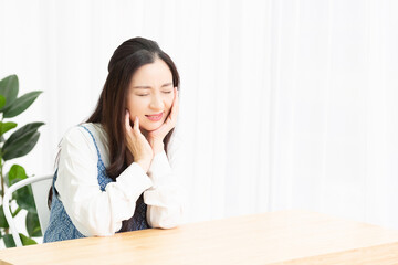 リビングで座りながら歯が痛くて頬に手を当てる主婦