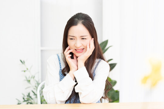 リビングで座りながら歯が痛くて頬に手を当てる主婦