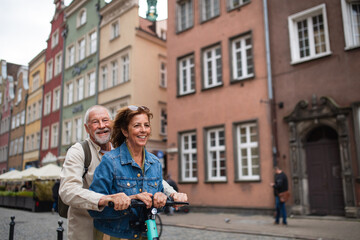 Obraz na płótnie Canvas Portrait of happy senior couple tourists riding scooter together outdoors in town