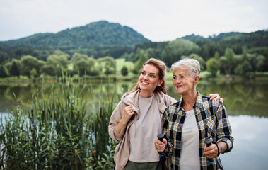 Happy senior mother embracing with adult daughter when standing by lake outdoors in nature