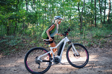 Active senior woman biker pushing ebike outdoors in forest.
