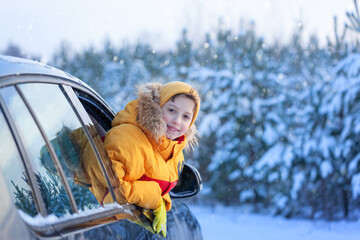 Winter holiday. Boy child is leaning out of the car window and enjoying snow road and forest winter.