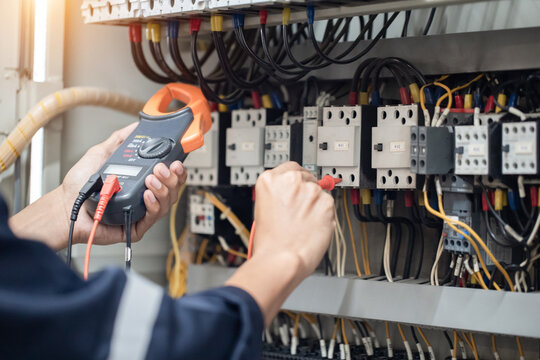Electrician engineer work tester measuring voltage and current of power electric line in electical cabinet control , concept check the operation of the electrical system .