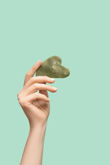 Female model hand with green jade gua sha scraper on green background. Spa body care tool. Beauty...