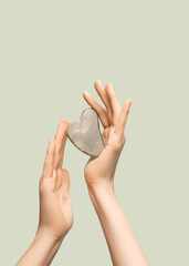 Female model hands with gray jade gua sha scraper on gray background. Spa body care tool. Beauty...