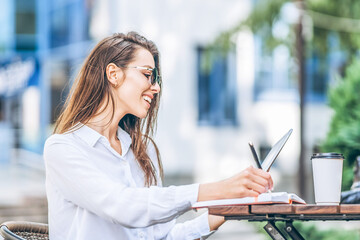 Young business woman drinking coffe and working on tablet in street cafe.