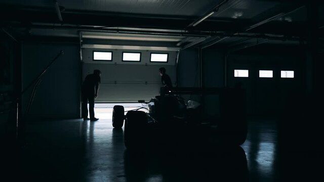 Garage with a racing car inside is getting closed by two men
