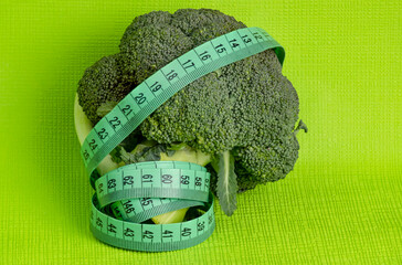 Broccoli and measuring tape on green background, weight loss concept