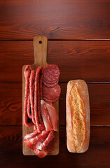 Various types of smoked meat and sausages are sliced on a cutting board. Nearby is a wheat bun. View from above. Vertical orientation.
