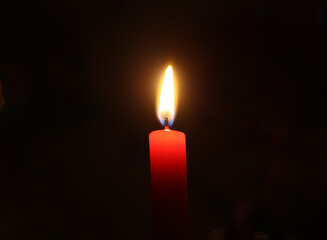 Red candle burning on decorated Christmas tree background. 
