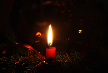 Red candle burning on decorated Christmas tree background. 