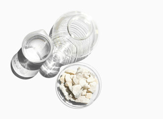 Closeup chemical ingredient on white laboratory table. Calcium carbonate Chip in Chemical Watch Glass place next to beaker with alcohol and Erlenmeyer flask. Top View