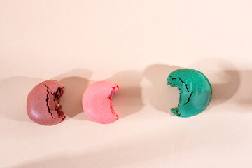 Colorful cake macaron bitten on beige background, pastel color.