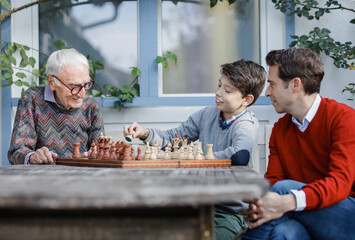 Man looking at father playing chess with son in backyard