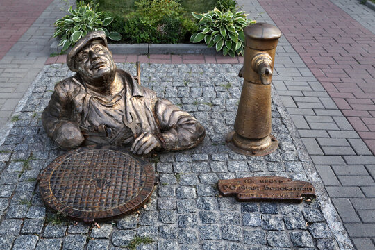 Cherkasy, Ukraine - August 14, 2021: A metal statue of a plumber looking out of a manhole near the central office of Cherkasy water and sewage services.