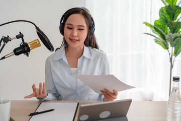 Bright Asian women record a podcast with a microphone and computer camera. A young woman work from...