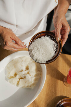 Woman with grated coconut plate preparing panellets in kitchen