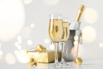 New Year champagne in wineglasses and bottle in bucket decorated festive Christmas gold baubles on white background. Close up. Holiday greeting card with copy space. Happy New Year 2022.