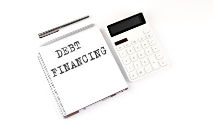 Notepad with text DEBT FINANCING with calculator and pen. White background. Business