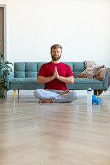 Yoga practice at home - middle aged man meditating while doing yoga. Full-length vertical photo.