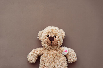 Ein kleiner brauner Teddybär mit einem Heftpflaster auf dem Arm und einem roten Herzen....