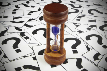 Hourglass on question marks background.	