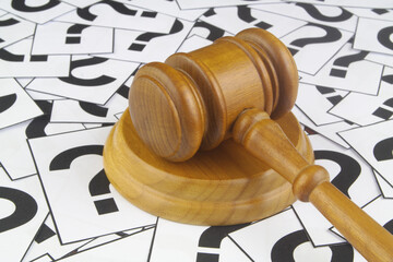 Legal questions and answers concept. Wooden judge gavel on question marks background.