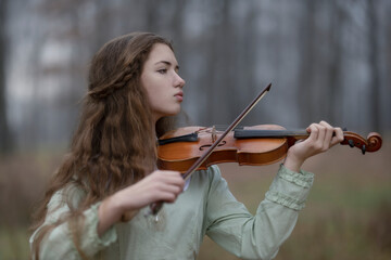The girl thoughtfully plays the violin in the  autumn forest