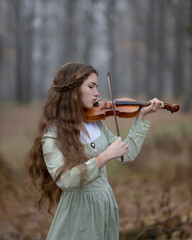 The girl thoughtfully plays the violin in the foggy autumn forest