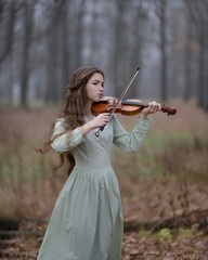 Young girl playing violin in autumn misty forest