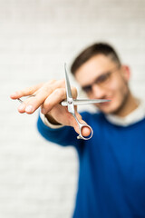 Barber hair dresser stylist in a blue shirt holds scissors for making a haircut blurred face