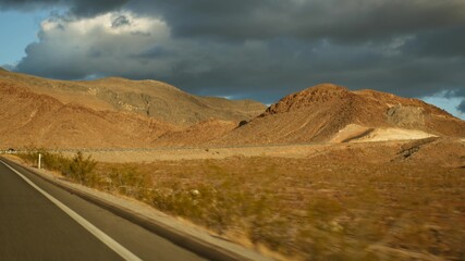 Road trip, driving auto from Death Valley to Las Vegas, Nevada USA. Hitchhiking traveling in America. Highway journey, dramatic atmosphere, sunset mountain and Mojave desert wilderness. View from car.