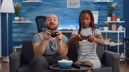 POV of interracial couple using controller for video game on television in living room. Young mixed race partners playing fun activity on console with joysticks at TV sitting on couch.