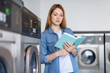 female student reading book while waiting in the launderette
