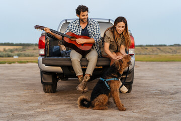 Young white couple playing guitar and stroking their dog