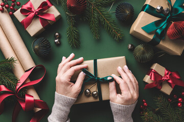 Overhead view on female hands tying velvet ribbon on Christmas gift box on green background.