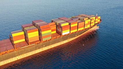 Aerial drone photo of huge container tanker ship carrying truck size colourful containers near Mediterranean port at sunset