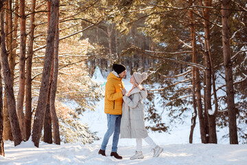 Good-looking couple spending time outdoors in winter in snowy forest, winter holidays. 