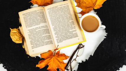 Naklejka na ściany i meble A cup of coffee with autumn leaves, glasses a book and a knitted scarf. Cozy home, autumn concept. Top view, flat lay.