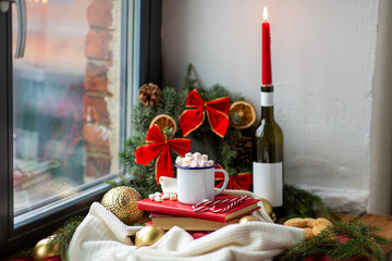 winter holidays concept - cup of whipped cream with marshmallow and candy canes, books, oatmeal cookies, candle burning in wine bottle and christmas decorations on window sill at home
