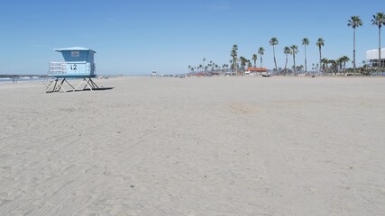 Tropical palm trees on white sandy beach by sea water waves, pacific ocean coast, Oceanside California USA. Blue sky and lifeguard tower. Life guard watchtower hut, summertime shore. Los Angeles vibes