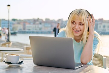 Smiling beautiful teenage girl in headphones looking into a laptop.