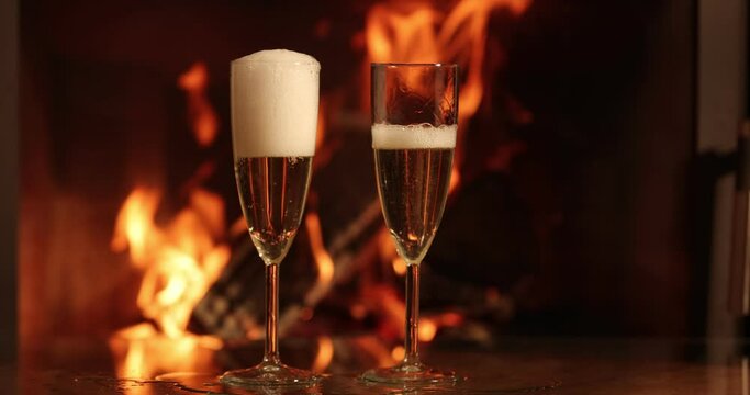 Champagne in two glasses on table in front of burning fireplace. 4k