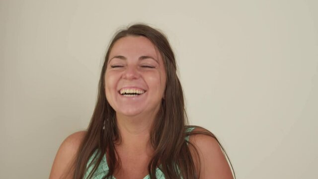 Portrait of cheerful plump young adult woman laughing, making spontaneous movements of face and body, expressing lively amusement, contempt or derision against white background