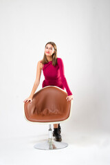 Young woman in stylish dress looking at the camera while posing leaning on a chair on an isolated background.