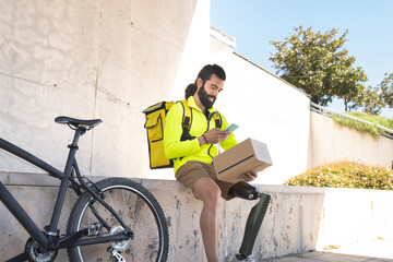 Smiling disabled delivery man scanning box with mobile phone by bicycle