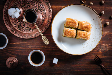 Turkish or Bosnian dessert called Baklava with pistachio served with traditional Turkish or Bosnian coffee set on a wooden board in moody atmosphere