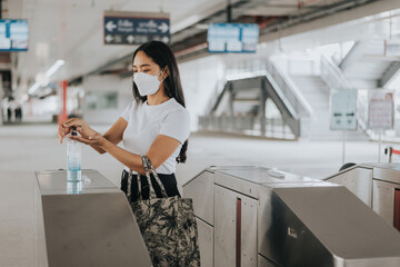 Asian woman wearing protective mask and washing hand with alcohol gel in train station. woman...